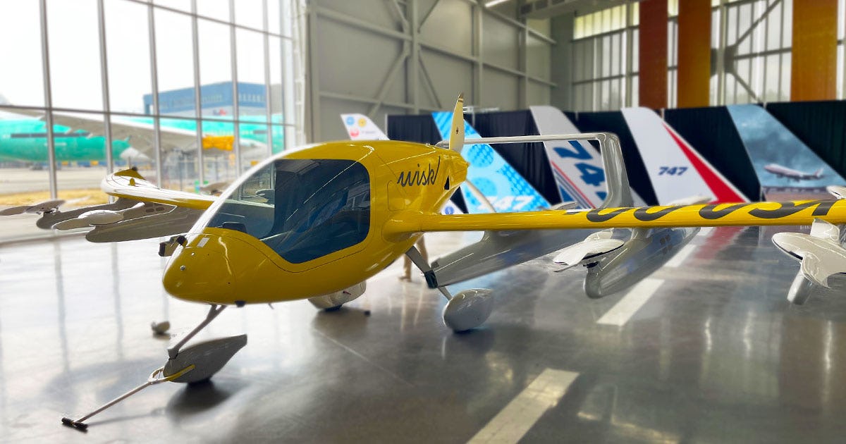 Wisk Aero Gen 5 displayed on the Boeing Future of Flight Gallery floor, with large hangar windows letting in sunlight from behind.