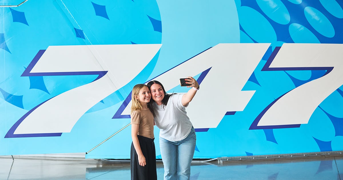 Two guest taking a selfie in front of a 747 tail's livery