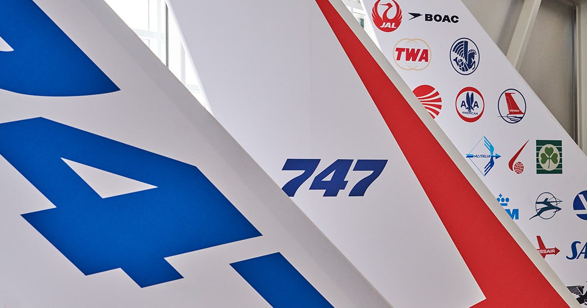 Small-scale recreations of Boeing 747 tail fins, showcasing design evolution from the first 747 to modern models. At right is a vertical stabilizer inspired by the original 747 (N7470), featuring its white-and-red livery and logos from early airline customers such as Pan Am, BOAC, TWA, and Japan Airlines. The center model reflects the actual first-generation tail fin, while the left shows the most recent design.