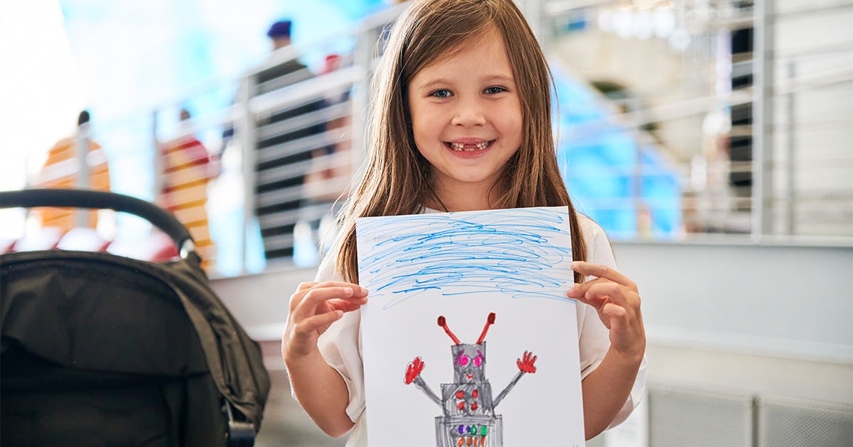 A smiling girl proudly holding up a completed drawing.