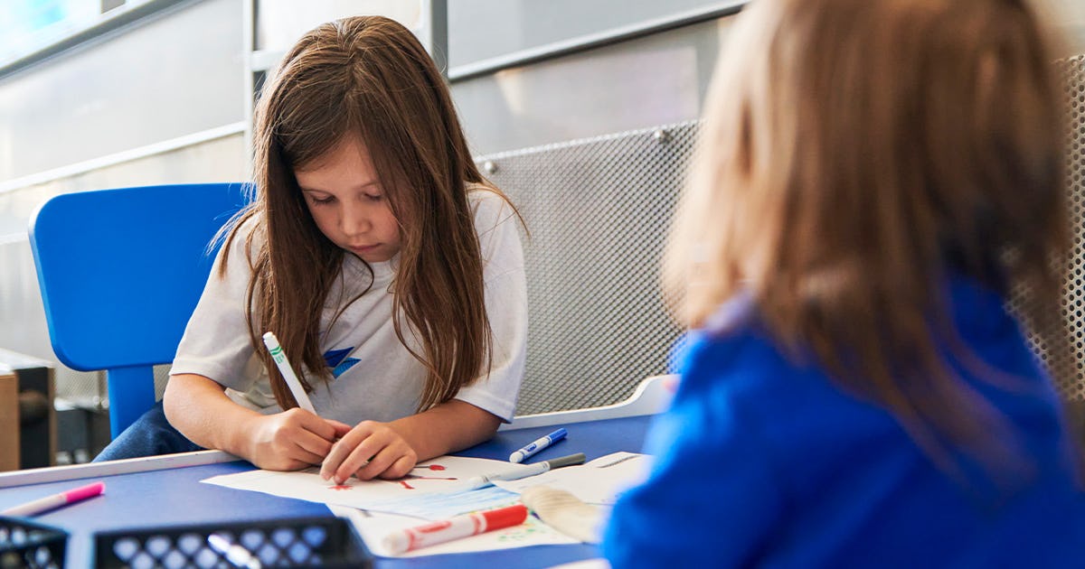 Two girls sitting at our Kids' Zone table working on a coloring activity.